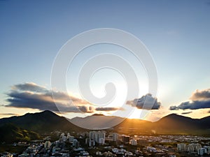 Aerial landscape photo of Recreio dos Bandeirantes beach during sunset, with the sun dipping behind the mountains and