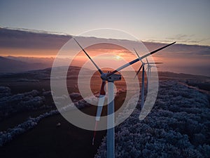 Aerial landscape photography of sunrise over frost-covered nature with wind turbines. Windmill in soft morning light