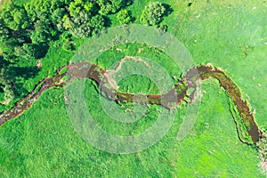Aerial landscape of winding small river, stream in green field, top view meadow