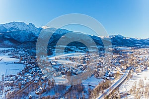 Aerial landscape of Zakopane, Poland during the winter season. Small houses and forest covered in snow with mountains in