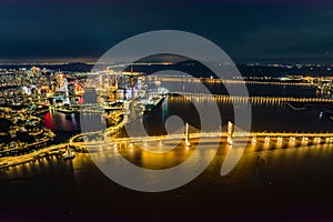 Aerial long exposure view of a futuristic illuminated city on an island with a bridge at night