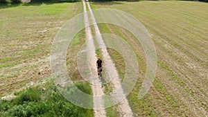 Aerial: man cycling along country road through cultivated fields and farmland, sunny day, eco friendly transportation on cycle lan