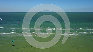 Aerial of many kiteboarders with colorful kites flying over the blue sea lagoon ride on kiteboards. Kitesurfers surf on