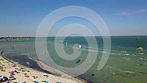 Aerial of many kiteboarders with colorful kites flying over the blue sea lagoon ride on kiteboards. Kitesurfers surf on