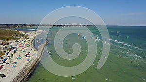 Aerial of many kiteboarders with colorful kites flying over the blue sea lagoon ride on kiteboards. Kitesurfers surf on