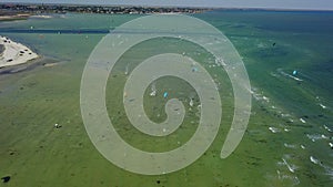 Aerial of many kiteboarders with colorful kites flying over the blue sea lagoon ride on kiteboards. Kitesurfers surf on