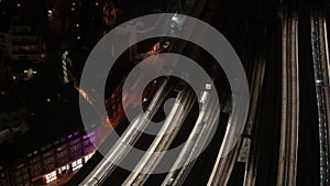 Aerial night view of train station, trains slowly moving from illuminated platforms, cars driving on streets