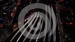 Aerial night view of train station, trains slowly moving from platforms, cars driving on streets, pedestrians walking on platforms