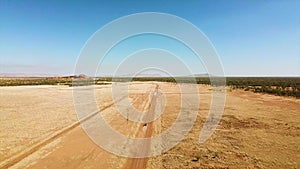 Aerial, offroad car speeds along desert road as drone rises to reveal arid landscape