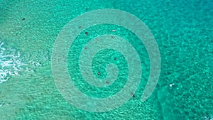 Aerial Pan Upwards shot of bodyboarders catching waves in clear tropical ocean