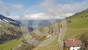 Aerial panorama of Alpine village on green mountain hills, cloudy sky, tourism