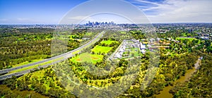 Aerial panorama of Eastern Freeway leading to Melbourne CBD skyscrapers on bright summer day.