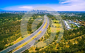 Aerial panorama of green parkland, Melbourne Polytechnic, and Melbourne CBD skyscrapers in the distance on summer day.