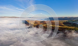 Aerial panorama of a narrow, winding mountain road emerging above a bank of fog in a rural valley