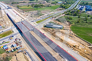 Aerial panorama top down view of an unfinished asphalt covered road with dirt, tracks of heavy machinery at construction site. The