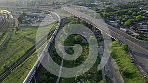 Aerial Panorama of transport highways: Electric train rides on rails, cars go on the highway at dawn. Shot on Drone.