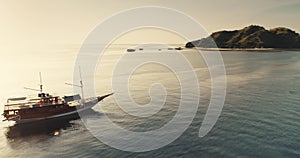 Aerial panorama: two yachts sailing near tropical island. Sunset sun reflect in calm sea water