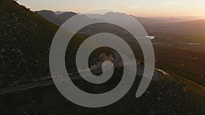 Aerial panoramic footage of landscape at sunset time. Road leading around mountain high above wide valley. South Africa