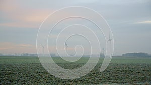 Aerial panoramic landscape of green meadow and windmills on foggy day. Amazing view on wind turbines generating energy