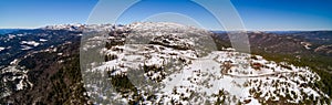 An aerial panoramic shot of snow covered mountain with trees and road going down the sides