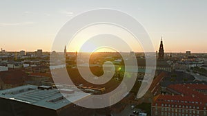 Aerial panoramic view of buildings in city centre against setting sun. Silhouettes of towers protruding above town