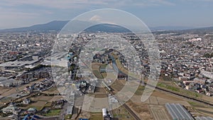 Aerial panoramic view of city. Commuter train passing on railway line in suburbs. Iconic Mount Fuji in distance. Japan