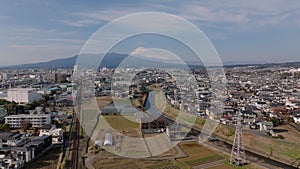 Aerial panoramic view of city with residential urban borough and Fujisan snowcapped mountain in distance. Descending