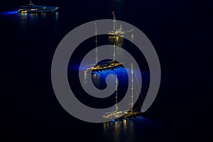 Aerial panoramic view of luxury mega yacht with night illumination, long exposure, tall masts, boat is moored in sea