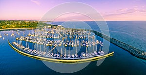 Aerial panoramic view of moored sailboats, breakwater, and Melbourne coastline at beautiful sunset.