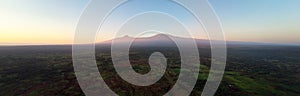 Aerial, panoramic view on Mount Kilimanjaro volcano, summit covered in snow lit by first sun rays with masai villages with