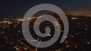 Aerial panoramic view of night city. Streets and buildings in urban borough, glowing harbour in background. Barcelona