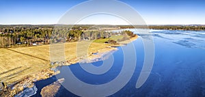 Aerial panoramic view over Swedish village and crystal clear frozen lake in Northern Scandianvia. Blue ice, clear skies, sunny