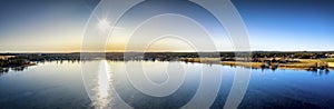 Aerial panoramic view over Swedish villages and crystal clear frozen lake in Northern Scandianvia. Sun in clear sky, blue ice,