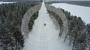 Aerial panoramic view of the only red car on the road in the beautiful winter landscape of Lapland during a snowfall.