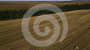 Aerial panoramic view of the tractor is working on wheat field with haystacks