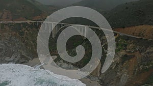 Aerial panoramic view of vehicles driving over Bixby Creek Bridge. Amazing concrete construction high above valley at