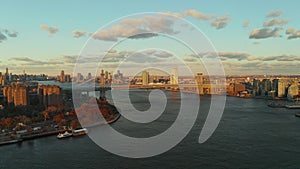 Aerial panoramic view of Williamsburg Bridge over wide river in city. Buildings lit by setting sun. Brooklyn, New York