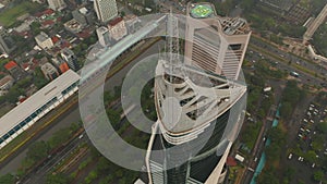 Aerial pedestal tilting into overhead view of the top of the Wisma 46 skyscraper in Jakarta, Indonesia on a cloudy day