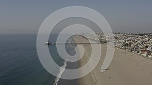 Aerial: people at the beach waves, water with pier in Los Angeles, California, Sunny, Blue Sky
