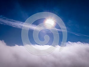 Aerial photo above clouds with halo around Sun, clear sky above fast moving white cloudscape