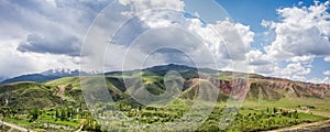 This aerial photo displays a vast valley encompassed by gentle hills and high mountains under a cloudy sky