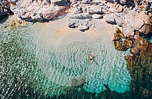 Aerial photo of man lying on the water in STAR pose on rocky pebbly beach and sun tanning. Soft waves washing his body on lonely