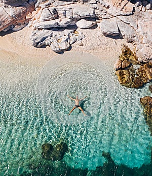 Aerial photo of man lying on the water in STAR pose on rocky pebbly beach and sun tanning. Soft waves washing his body on lonely