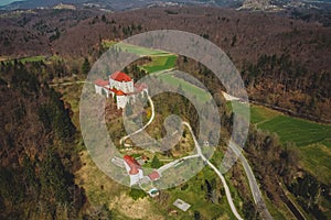 Aerial photo of Mirna castle in Dolenjska region of Slovenia is rising up from the trees on a castle hill on a sunny day with blue photo