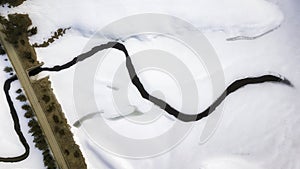 Aerial photo over winter mountain. Meandering river in show field near road.