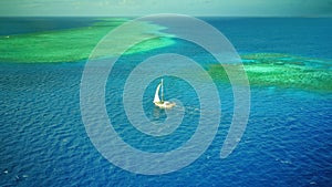 Aerial photo of a sailboat navigating through a tropical pass between reefs