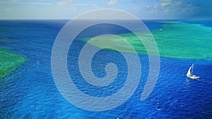 Aerial photo of a sailboat navigating through a tropical pass between reefs