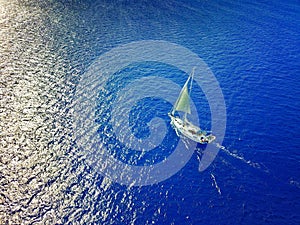 Aerial photo of a sailboat navigating through a tropical pass between reefs