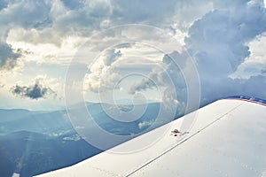 Aerial photo of a small plane wing and beautiful clouds in the sky and silhouettes of hills and meadows