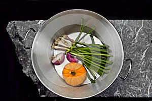 Aerial photo of a saucepan with vegetables on a stone slab.